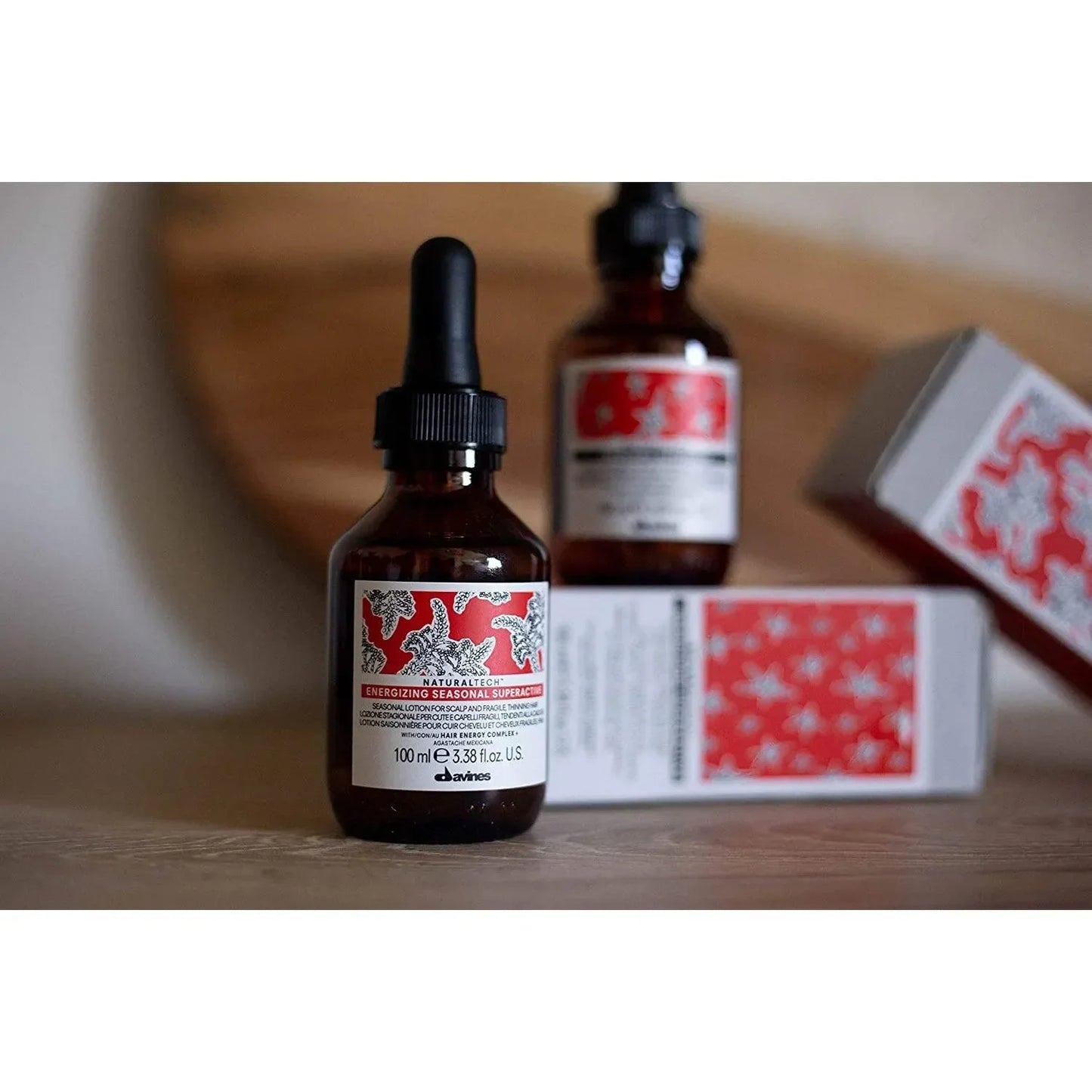 Davines Energizing Superactive Serum brown glass dropper bottle with red and white label on wooden surface, haircare product.