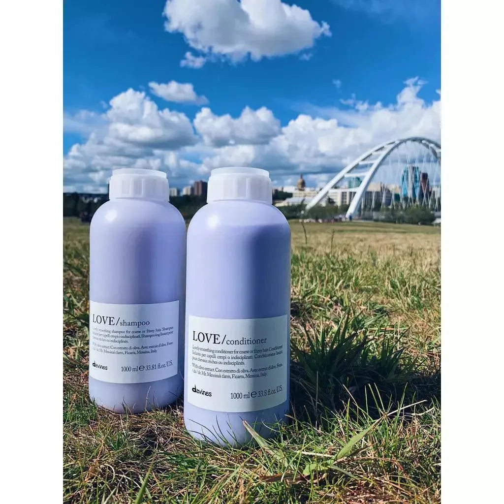 Davines LOVE Smoothing Shampoo and Conditioner large bottles outdoors on grass with city bridge background