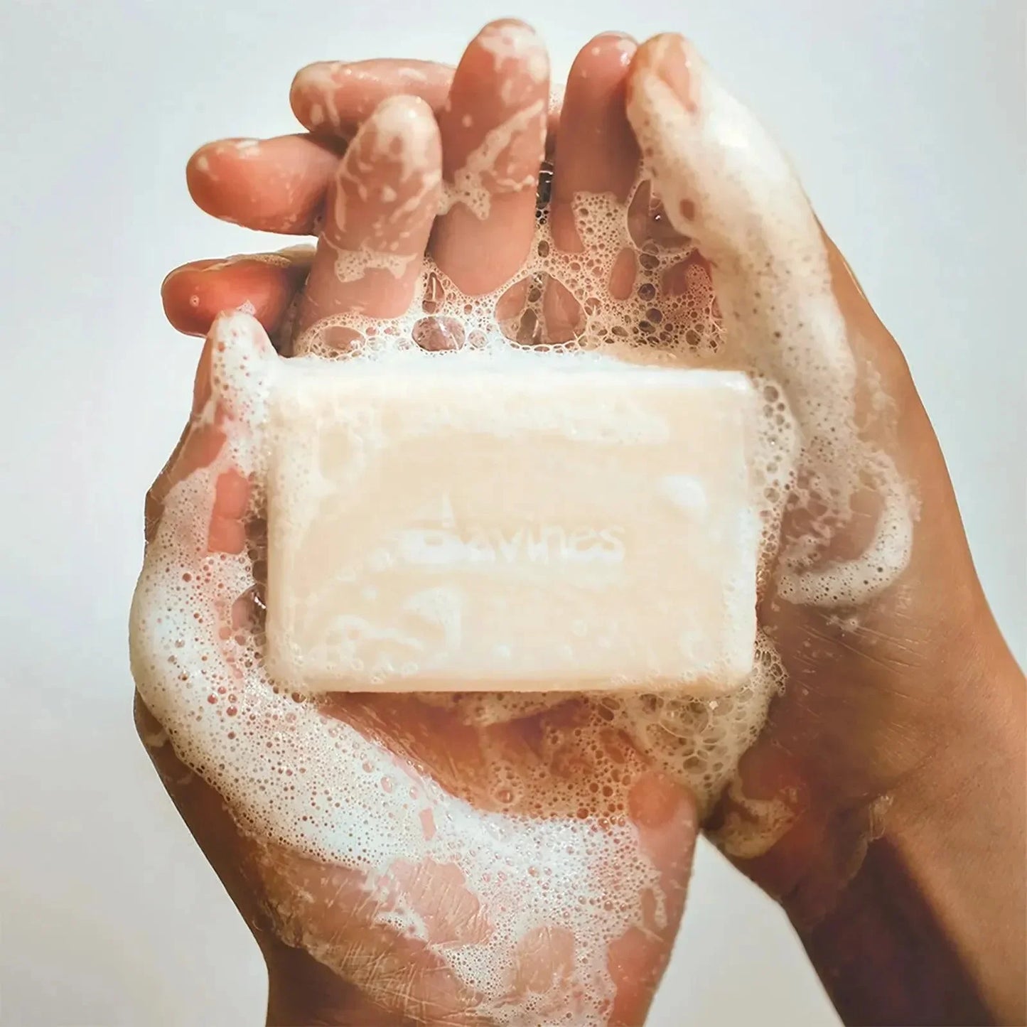 Hands holding a foamy solid shampoo bar, lathered with bubbles, close-up.