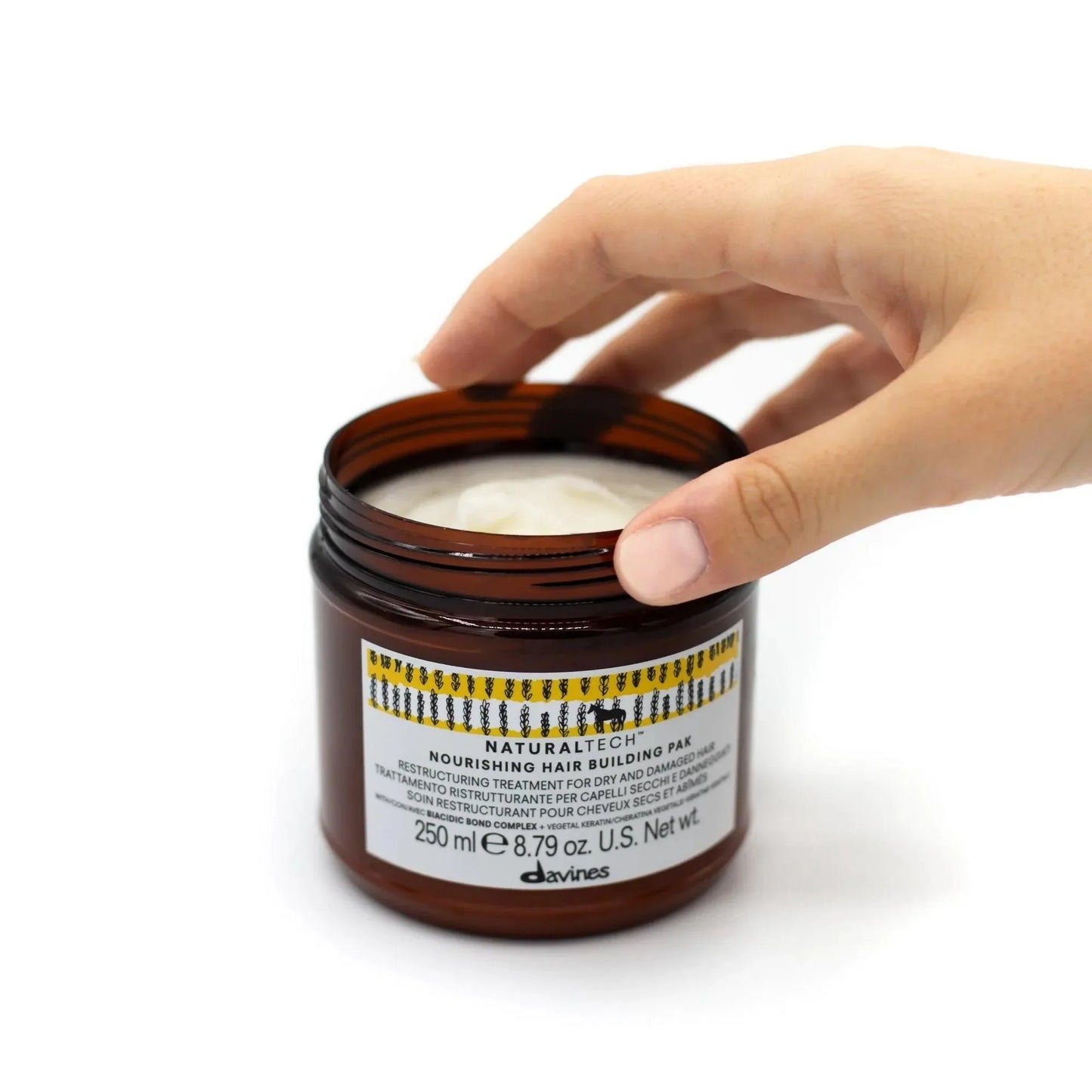Hand dipping into Davines Naturaltech Nourishing Hair Building Pak mask jar on white background