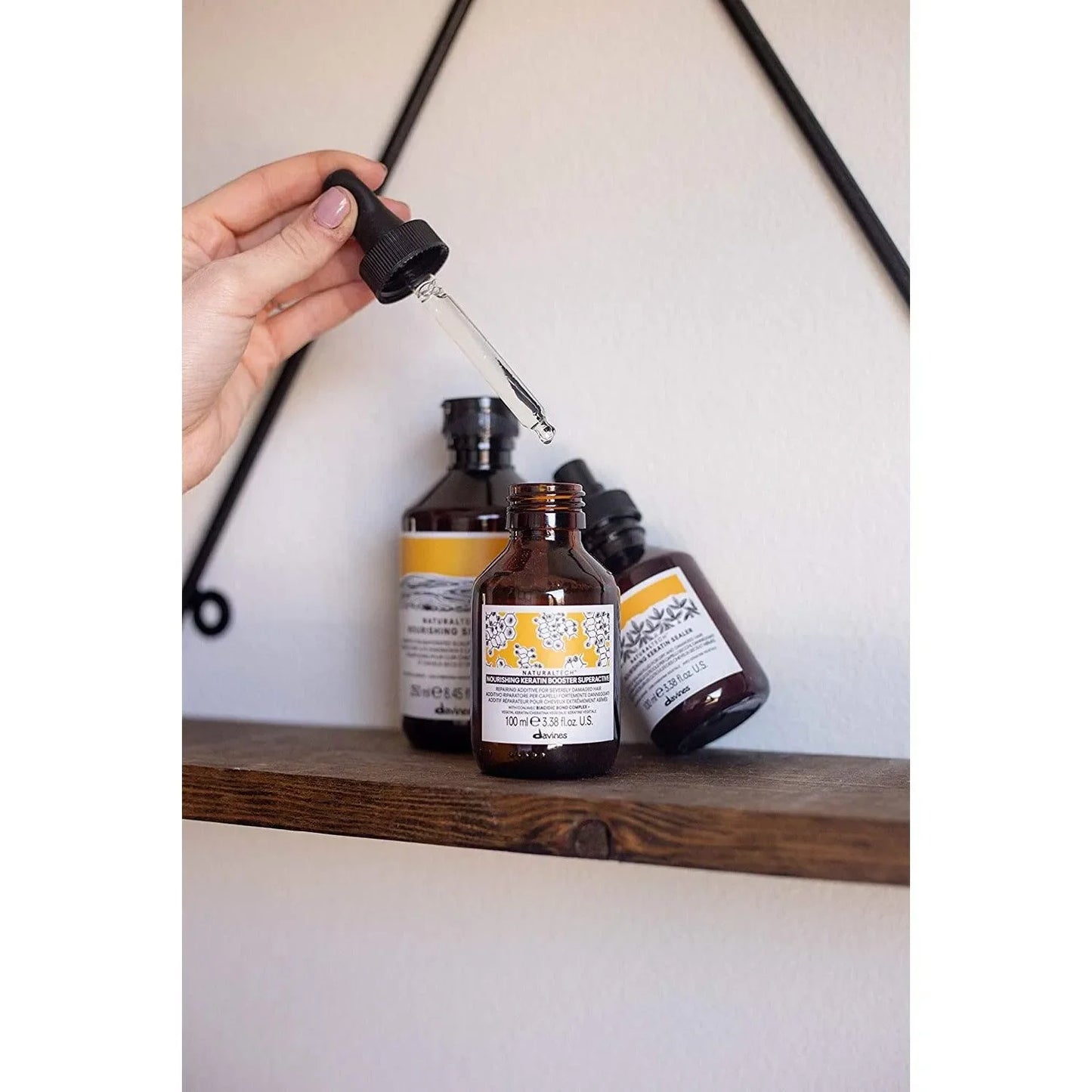 Hand using dropper with amber bottle of Davines nourishing keratin hair booster on shelf