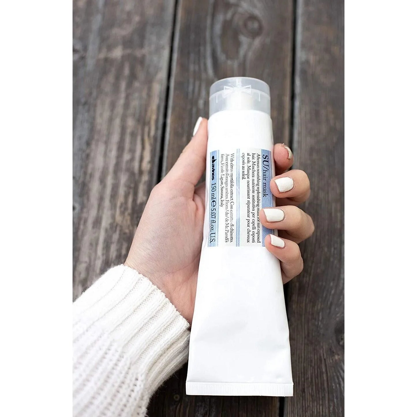 Hand holding Davines SU hair mask tube on wooden background, professional haircare product