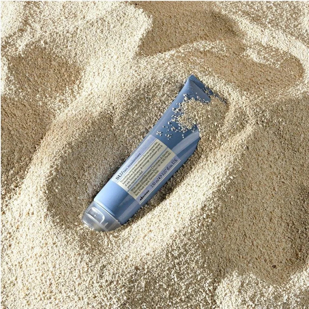Blue tube of sun care lotion partially buried in sand, beach sun protection product