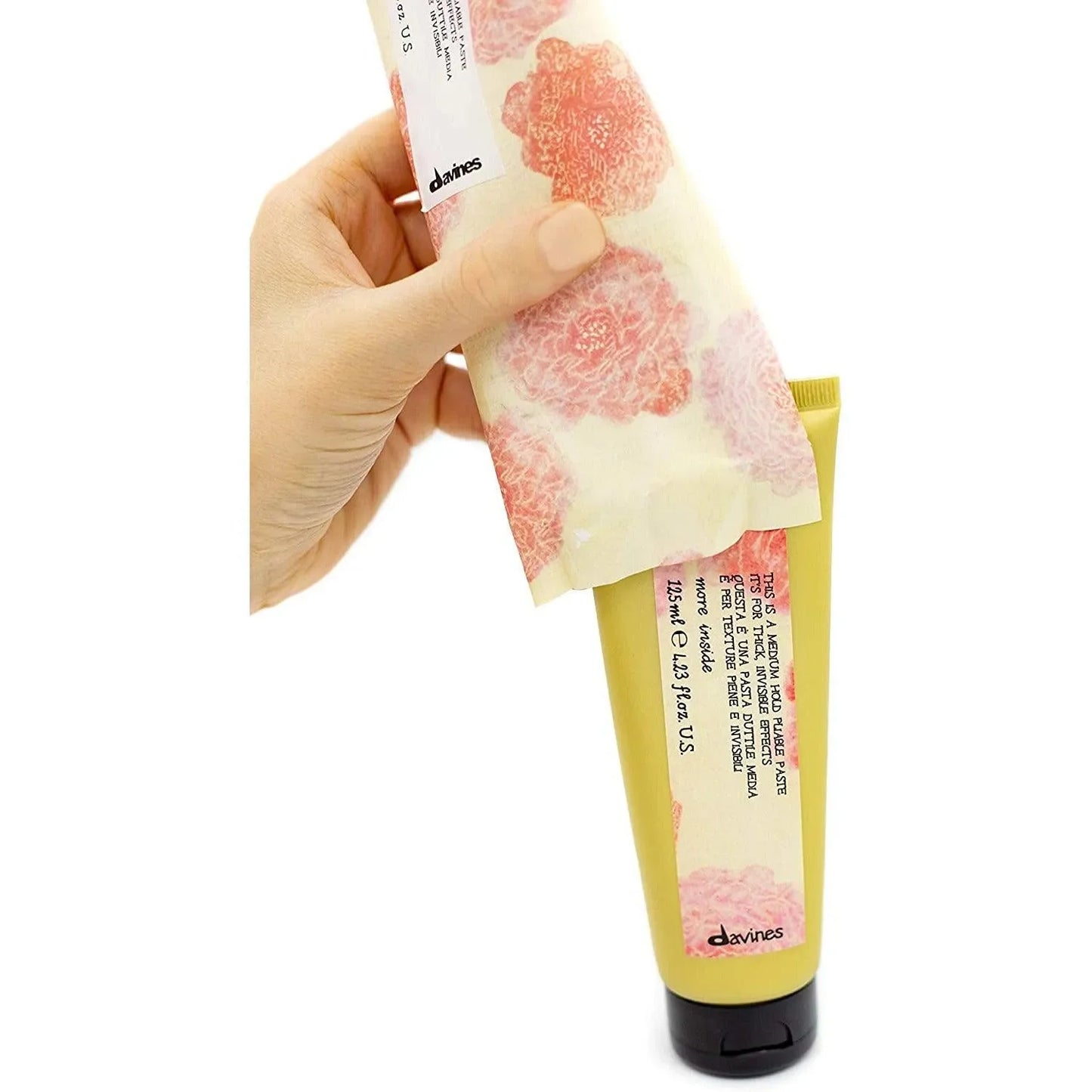Hand holding floral-wrapped tube of Davines medium hold pliable hair paste on white background
