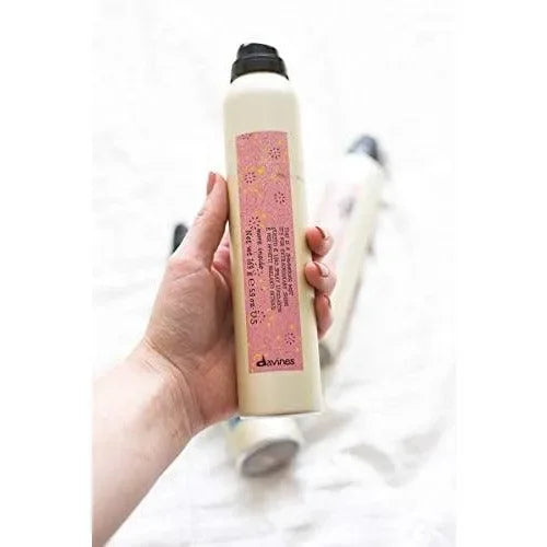 Hand holding a Davines hair mist spray bottle with pink label, haircare product visible