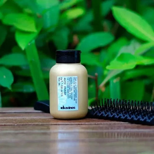 Texturizing hair dust bottle with black cap beside hairbrush on wooden surface, green leaves background