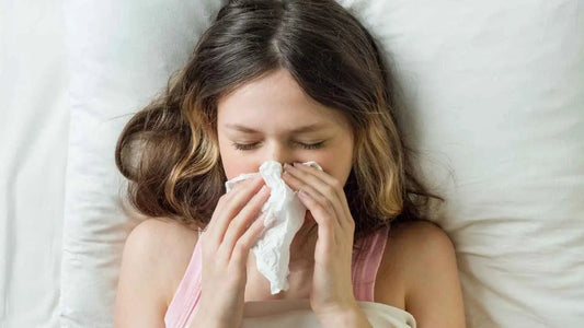 Young woman in bed blowing nose with tissue, illustrating weak immune system, Goldfarmaci