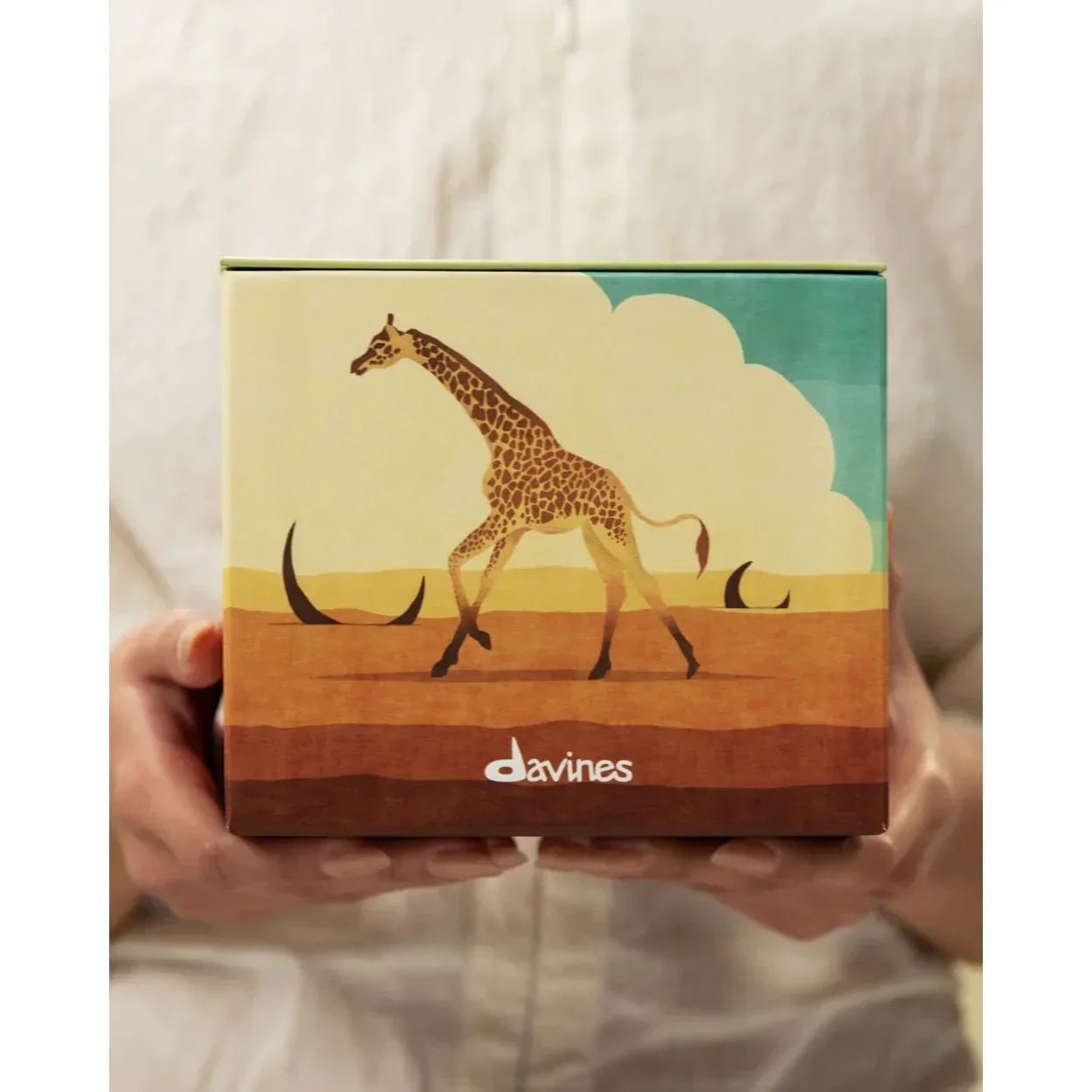 Person holding Davines Radiant Savanna gift box with giraffe illustration, Goldfarmaci skincare